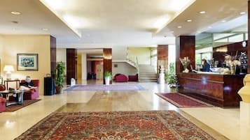 Un hall d’entrée spacieux, agrémenté d’un grand tapis décoratif, d’un comptoir de réception et d’un escalier menant aux étages supérieurs.