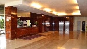 Een ruime lobby met een receptiebalie, een grote spiegel en een houten vloer.