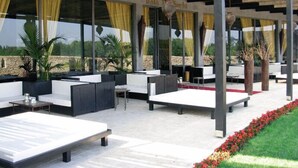 An outdoor seating area with tables and chairs, large windows with yellow curtains, and potted plants. - Amareclub Baia Dei Turchi Resort - Adults Only (Otranto)
