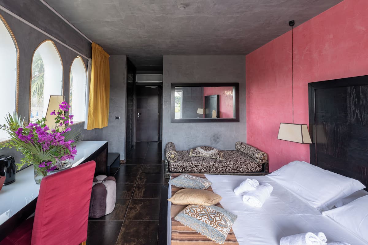 Una habitación de hotel con una cama, un sofá, un escritorio con un florero y un espejo grande en la pared.