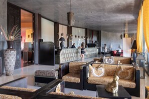 Um lobby moderno com sofás estampados, balcão de recepção e luminárias pendentes.
