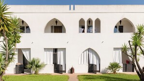 Un edificio con diverse finestre ad arco e porte, circondato da vegetazione e palme.