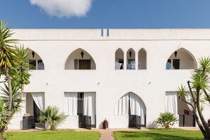 A building with multiple arched windows and doors, surrounded by greenery and palm trees. - Amareclub Baia Dei Turchi Resort - Adults Only (Otranto)