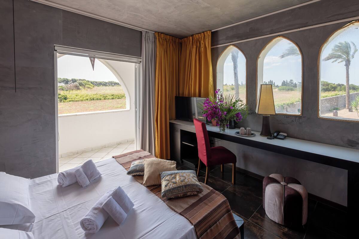 Una camera d'albergo con un letto, una scrivania con un computer, una sedia e vista sull'esterno.