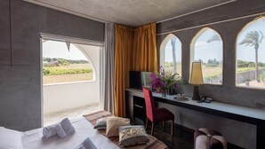 A hotel room with a bed, a desk, a chair, a TV, and a view of the outdoors. - Amareclub Baia Dei Turchi Resort - Adults Only (Otranto)