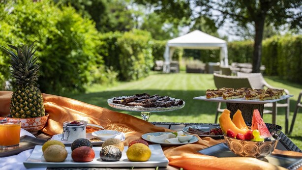 An outdoor dining setup with a variety of food items, including pastries, fruits, and desserts, arranged on a table with a view of a garden and a gazebo in the background. - B&B Hotel Remilia (Bibbiano)