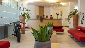 A reception area with a motorcycle, red seating, and potted plants. - B&B Hotel Remilia (Bibbiano)