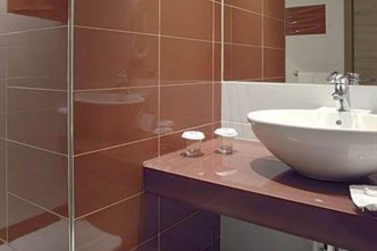 A modern bathroom with a large sink, a mirror, and a white stool.