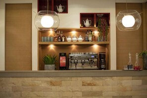 A bar area with a coffee machine, shelves with bottles, and hanging lights.