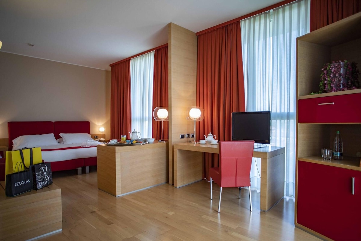 Ein Hotelzimmer mit Bett, Schreibtisch, Computer, Stuhl und Fernseher.