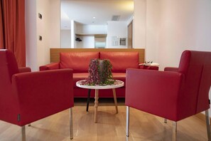 Una habitación moderna con un sofá rojo, dos sillones rojos, una mesita redonda con un florero y piso de madera.