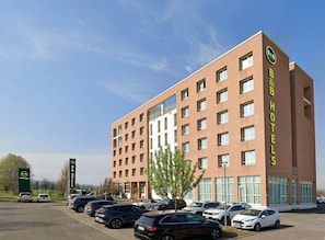 Ein Bed and Breakfast Hotel mit mehreren Etagen, einem Parkplatz mit einigen Autos und wolkenlosem Himmel.
