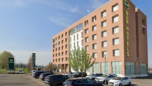 A B&B hotel with multiple floors, a parking lot with several cars, and a clear sky. - B&B Hotel Remilia (Bibbiano)