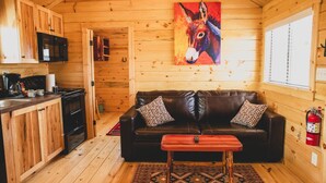 A cozy cabin with a wooden interior, a black leather sofa, a wooden coffee table, and a vibrant donkey painting on the wall. - Amarillo by Morning (Amarillo)