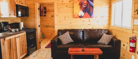 A cozy cabin with a wooden interior, a black leather sofa, a wooden coffee table, and a vibrant donkey painting on the wall.