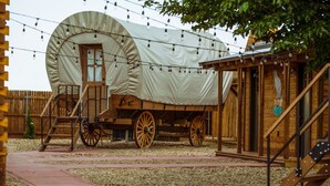 A covered wagon with a wooden structure, a wooden fence, and a gravel path. - Amarillo by Morning (Amarillo)