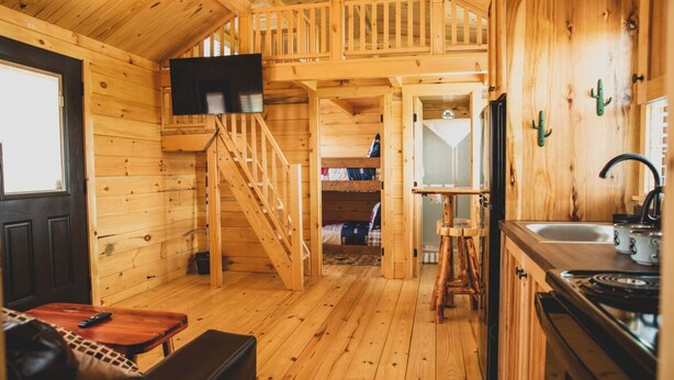 A wooden cabin interior with a kitchen, dining area, and a staircase leading to a loft bedroom. - Amarillo by Morning (Amarillo)