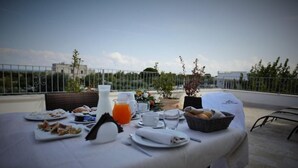 Une table de petit-déjeuner installée sur une terrasse, offrant une vue sur les toits de la ville, avec une clôture et des bâtiments en arrière-plan.