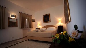 Een slaapkamer met een bed, nachtlampjes, een nachtkastje, een lijst met een afbeelding en een vaas met bloemen.