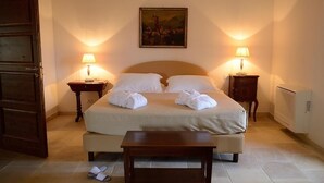 Un lit bien fait, avec du linge de lit et des serviettes blanches, deux tables de chevet avec des lampes, un tableau au mur et un banc en bois devant le lit.