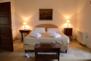 Ein ordentlich bezogenes Bett mit weißen Leinen und Handtüchern, zwei Nachttische mit Lampen, ein Bild an der Wand und eine Holzbank vor dem Bett.
