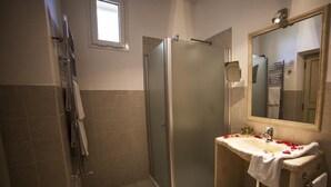 Une salle de bain avec une douche à parois de verre, un lavabo décoré de pétales de rose et un miroir.