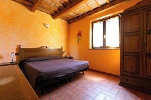 A bedroom with a wooden bed, a nightstand with a lamp, a wardrobe, and a window with curtains. - Il Podere del Germano Reale (Coriano)