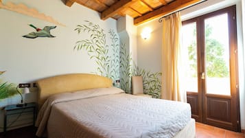 A bedroom with a bed, a nightstand, a wall-mounted lamp, a large window with curtains, and a wooden ceiling.