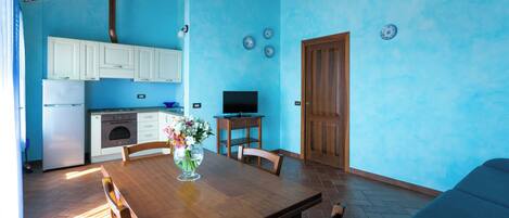 A compact kitchen with white cabinets, a wooden dining table, and a vase with flowers.
