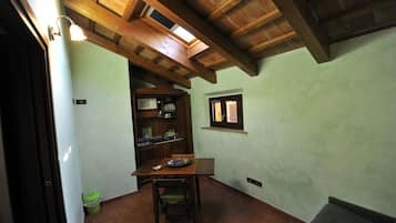 Una habitación con techo de madera, una mesa de comedor con sillas, una ventana pequeña y un bote de basura verde.