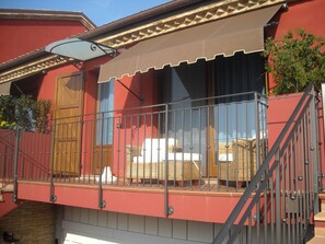 A red building with a covered balcony, wicker furniture, and a metal railing. - Il Podere del Germano Reale (Coriano)