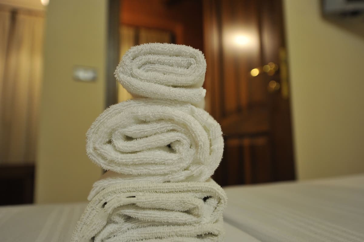 A stack of white towels on a bed in a hotel room.