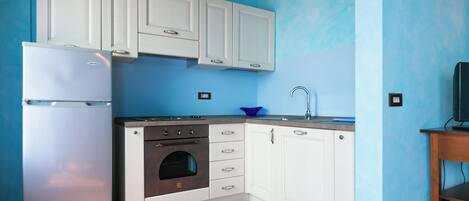 A compact kitchen with white cabinets, a stainless steel refrigerator, an oven, and a sink.