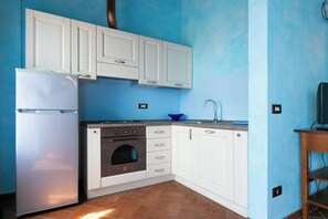 A compact kitchen with white cabinets, a stainless steel refrigerator, an oven, and a sink. - Il Podere del Germano Reale (Coriano)