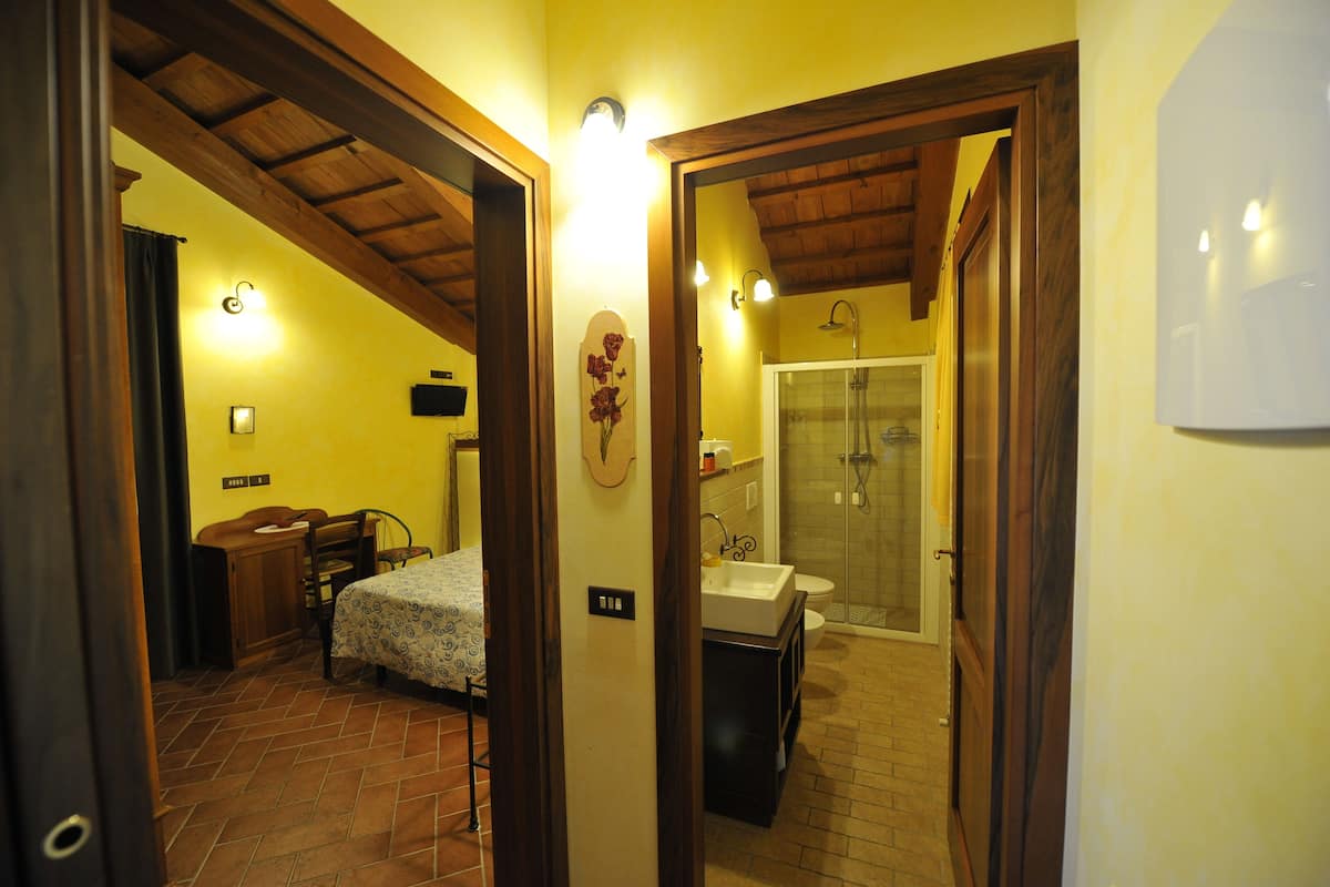 A bedroom with a bed, a desk, and a chair. There is a bathroom with a sink, toilet, and shower.