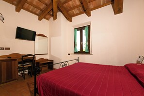A bedroom with a bed, a desk, a chair, a TV, and a window with curtains. - Il Podere del Germano Reale (Coriano)