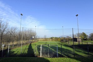 A tennis court with a net, surrounded by a fence, and two floodlights. - Il Podere del Germano Reale (Coriano)