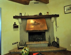 A fireplace with a decorative copper mantel, a small shelf with various items, and a vase of flowers on the mantel. - Il Podere del Germano Reale (Coriano)