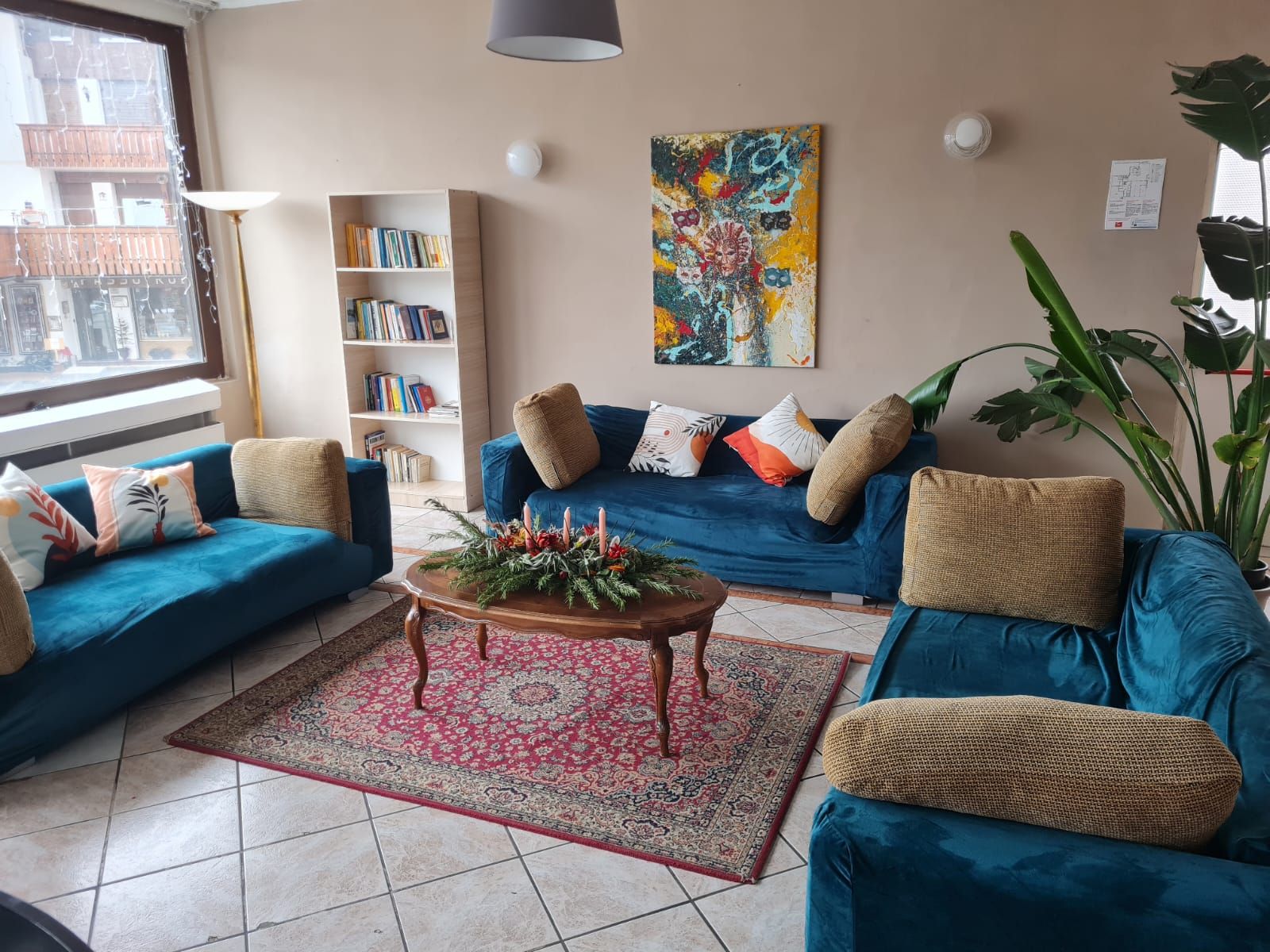 A living room with a blue sofa set, a bookshelf, a colorful abstract painting, and a large plant.