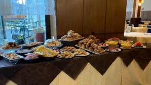 Una mesa de buffet con diferentes opciones de comida, incluyendo pasteles, frutas y postres, cubierta con un mantel marrón y blanco.