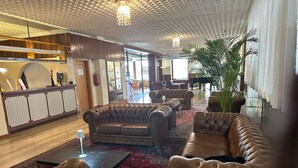 Eine Lobby mit Ledersofas, einem Empfangstresen, einem Flügel und einer großen Pflanze.