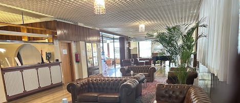 A lobby with leather sofas, a reception desk, a grand piano, and a large plant.