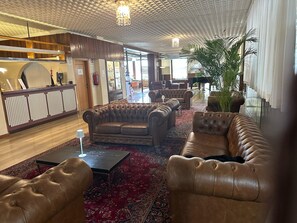 Eine Lobby mit Ledersofas, einem Empfangstresen, einem Flügel und einer großen Pflanze.