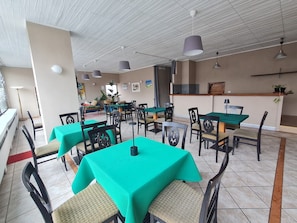 Un restaurant dont les tables sont recouvertes de nappes vertes, avec des chaises noires et des luminaires suspendus.