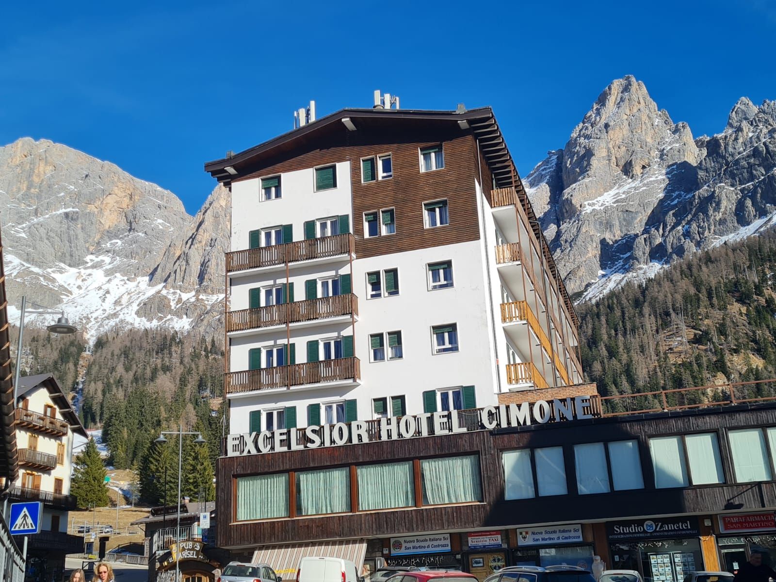 Un hôtel à plusieurs étages doté de balcons, situé dans une région montagneuse où l’on aperçoit les sommets au loin.