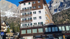 Ein mehrstöckiges Hotel mit Balkonen in einer gebirgigen Gegend, im Hintergrund sind Berggipfel sichtbar.