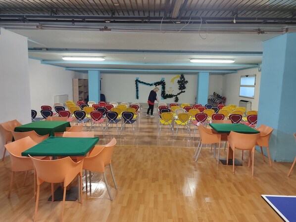 A conference room with rows of chairs and tables, a person cleaning, and a Christmas tree decoration. - Excelsior Hotel Cimone Lowcost (Primiero San Martino di Castrozza)