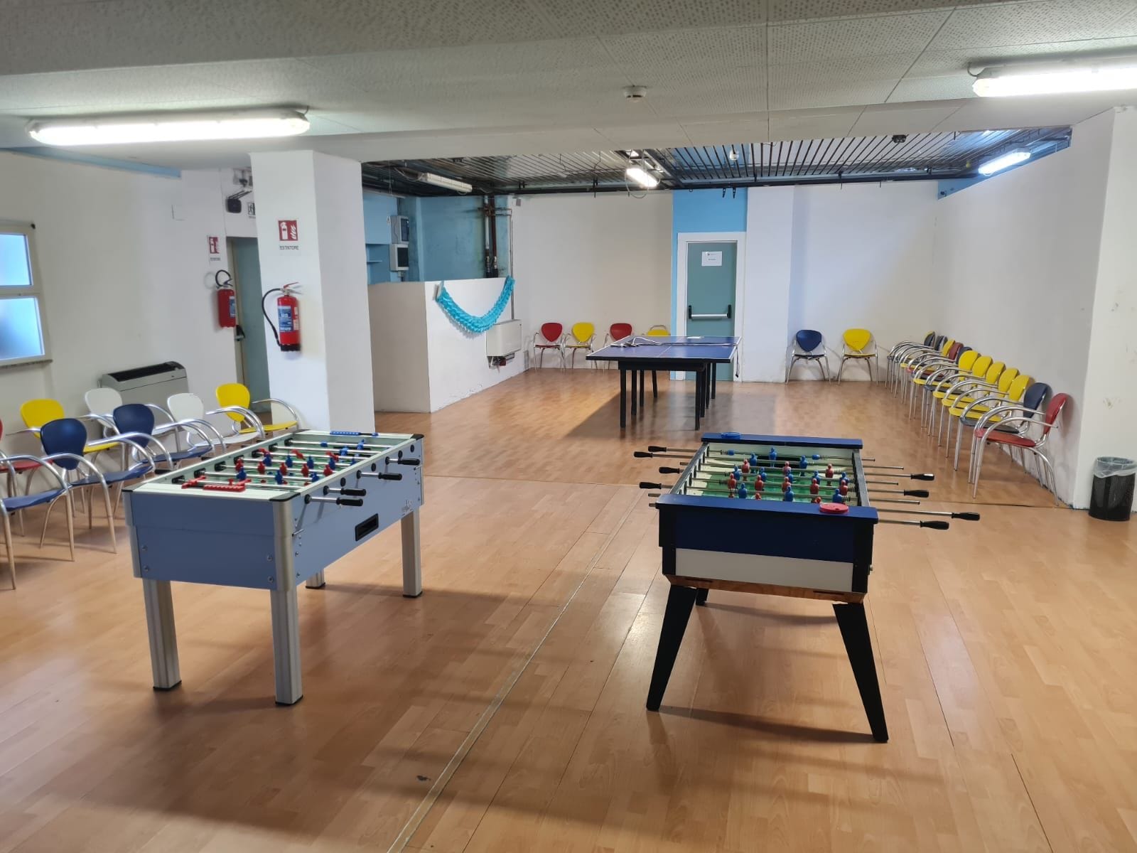 Una stanza con due tavoli da calcio, sedie, un estintore e una tenda blu.