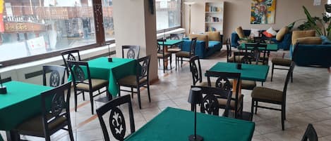 Um restaurante com mesas e cadeiras verdes, um sofá e uma estante de livros.