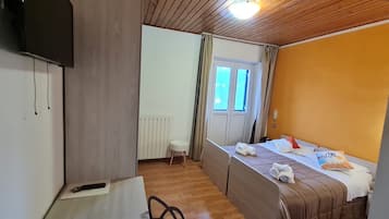 Una stanza con un letto, una scrivania, una sedia, un termosifone, una finestra e una televisione.